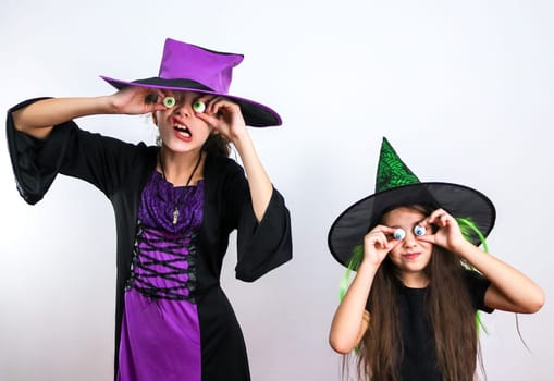 Two caucasian girls in witch costumes hold candies on their hands in front of their eyes and express halloween emotions, close-up side view.