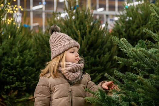 Small girl of three years old chooses a Christmas tree in the market.