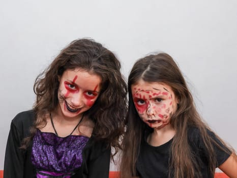 Portrait of two beautiful Caucasian girl sisters in black witch clothes with festive and bright makeup on their faces looking at the camera and making grimaces, close-up side view.
