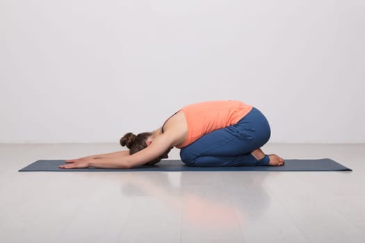 Beautiful sporty fit yogini woman practices yoga asana balasana (child's pose) - resting pose or counter asana for many asanas in studio