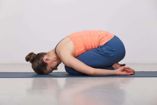 Beautiful sporty fit yogini woman practices yoga asana balasana (child's pose) - resting pose or counter asana for many asanas in studio