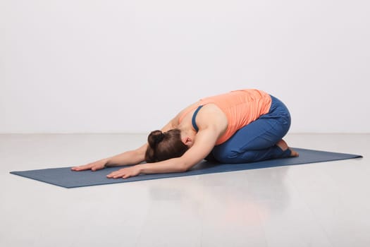 Beautiful sporty fit yogini woman practices yoga asana balasana (child's pose) - resting pose or counter asana for many asanas in studio