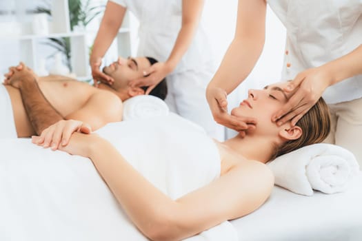 Caucasian couple enjoying relaxing anti-stress head massage and pampering facial beauty skin recreation leisure in dayspa modern light ambient at luxury resort or hotel spa salon. Quiescent