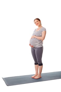 Pregnant smiling woman standing on yoga mat embracing her belly isolated on white background