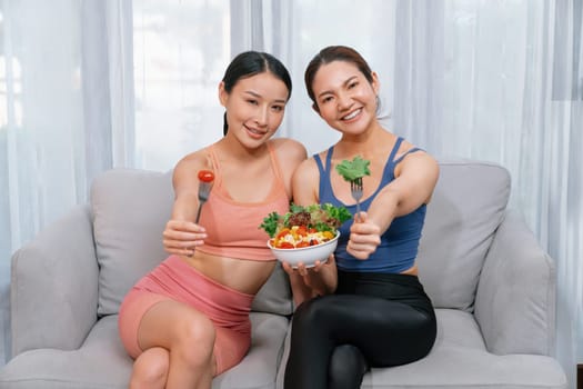 Young sporty Asian women in sportswear holding salad bowl together fill with vibrant of fruit and vegetable. Natural youthful and fit body lifestyle with balance nutrition and home exercise. Vigorous