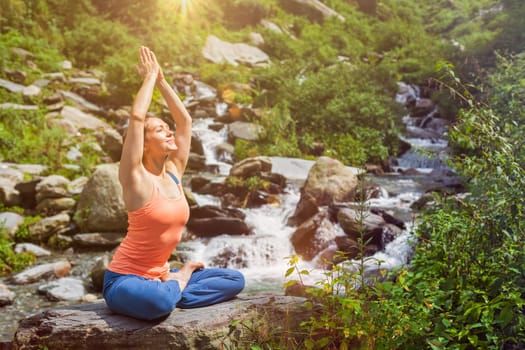 Woman in Hatha yoga asana Padmasana outdoors at tropical waterfall