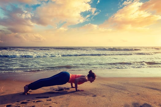 Vintage retro hipster effect image of woman practices Ashtanga Vinyasa yoga - Surya Namaskar Sun Salutation asana Chaturanga Dandasana four-limbed staff pose on sunset. Varkala beach, Kerala, India