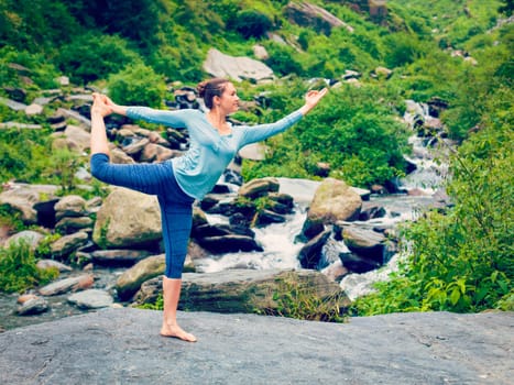 Vintage retro effect hipster style image of woman doing yoga asana Natarajasana - Lord of the dance pose outdoors at waterfall in Himalayas