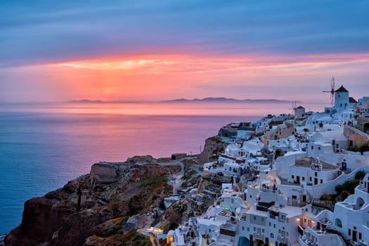 Famous greek iconic selfie spot tourist destination Oia village with traditional white houses and windmills in Santorini island on sunset in twilight, Greece