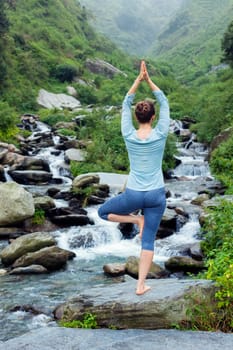 Woman in Hatha yoga balance yoga asana Vrikshasana tree pose at waterfall outdoors