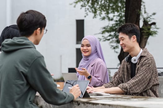 A group of happy multiracial students at the college with Muslim and Asian students grouped together sat on benches in the campus break area. Read books or study for exams together..