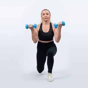 Full body length shot active and sporty senior woman lifting dumbbell during weight training workout on isolated background. Healthy active physique and body care lifestyle for pensioner. Clout