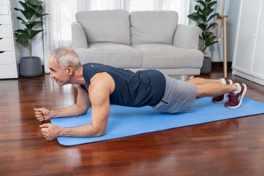 Athletic and sporty senior man planking on fitness exercising mat at home exercise as concept of healthy fit body lifestyle after retirement. Clout