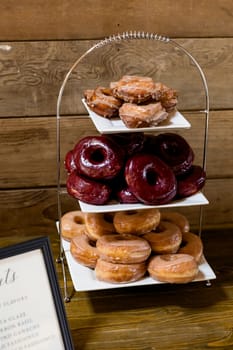 Wedding reception dessert bar buffet with donuts and other treats on stands for guests.
