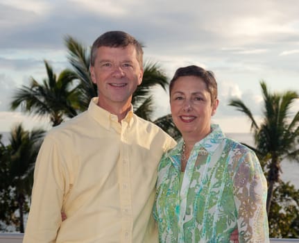 Smiling retired couple smiling as the sun sets behind over the palm lined ocean