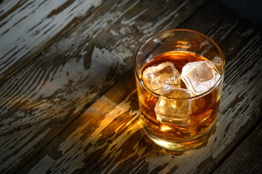A refreshing beverage with ice cubes glistens softly on a weathered wooden surface, inviting relaxation.