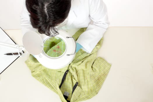 A forensic investigator observes and obtains samples from a shirt for further analysis.