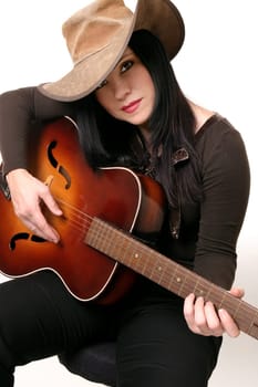 A woman sitting on a stool, playing an acoustic guitar