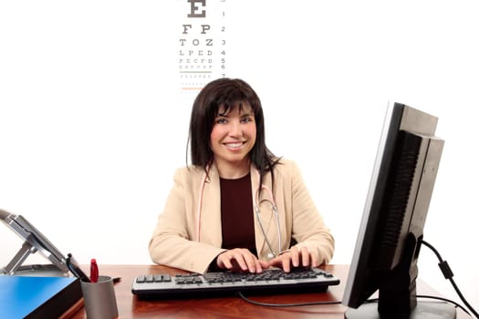 Smiling female doctor sitting at desk and using computer.
