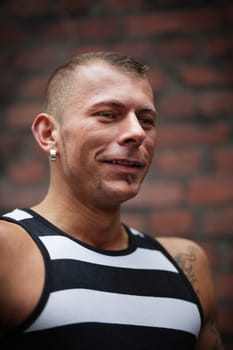 Smiling muscular man standing against a brick wall  selective focus