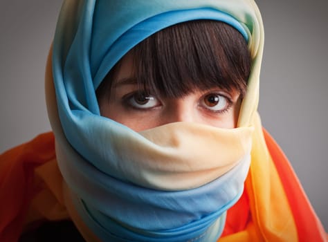 Brunette girl in multicolored head scarf  photographed on gray background