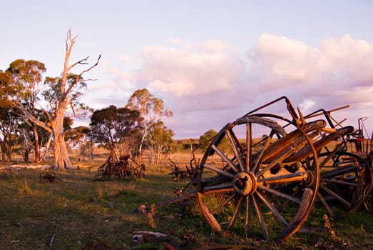 the old cart with broken wheels amongst other machinery in the paddock of the farm