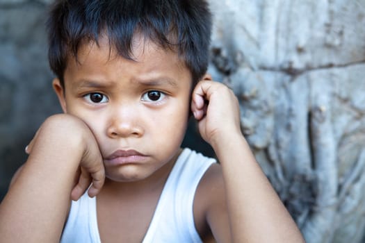 Poverty - portrait of a cute young Asian boy, Filipino male against wall with copyspace.
