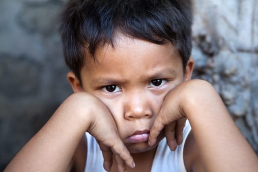 Young Filipino boy with sad expression against wall - poverty in the Philippines.