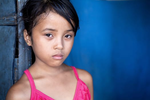 Young Filipina girl 8 years old with sad and somber expression over blue, poverty in the Philippines.