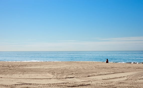 a single woman sits alone on the beach in california