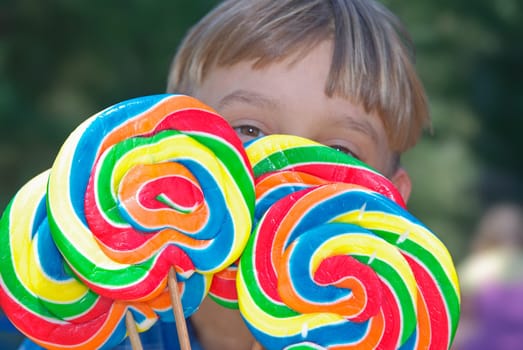 young boy looks over the top of four huge lollipops