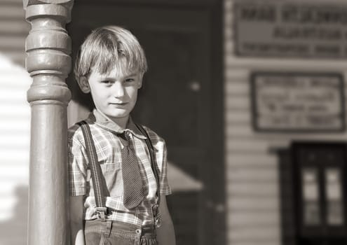 silver gelatin black and white of a young boy in tie and braces stands in front of an old shop