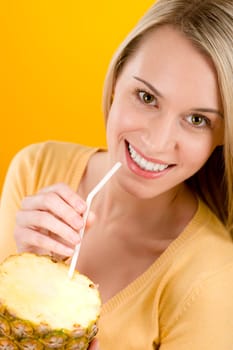 Healthy lifestyle - woman drink juice from pineapple with straw on yellow background