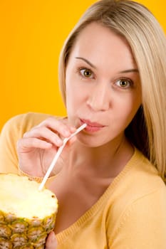 Healthy lifestyle - woman drink juice from pineapple with straw on yellow background