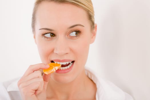 Healthy lifestyle - portrait of woman biting tangerine slice on white background