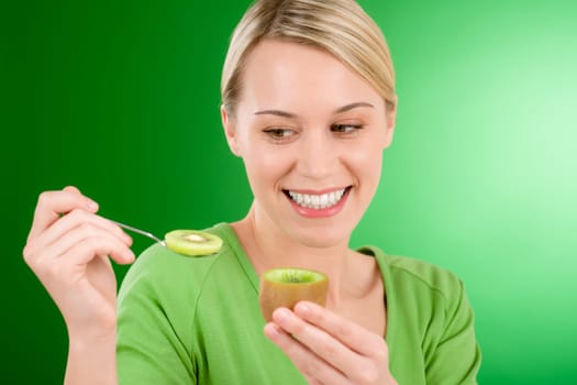 Healthy lifestyle - happy woman holding kiwi and teaspoon on green background