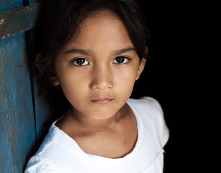Young Asian girl portrait - child from Philippines against blue door and black background.