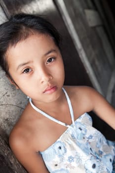 Young Philippine girl from impoverished neighborhood against wall.