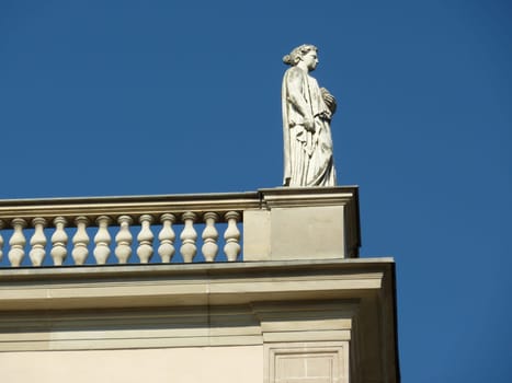 White statue of a woman standing upon the balcony at the top of a building and beautiful blue sky