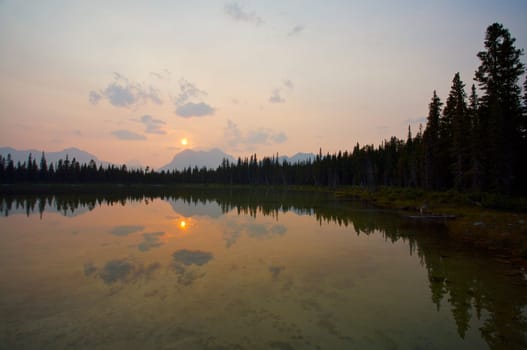 Sun setting over distant mountains and reflected in Buller Lake Rocky Mountains of Canada