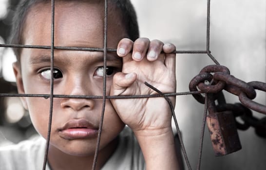 young Asian boy behind fence, slight grain, focus on hand
