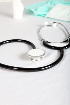 A stethoscope in the doctor's room lies on the table. Behind it is a face mask and a bandage