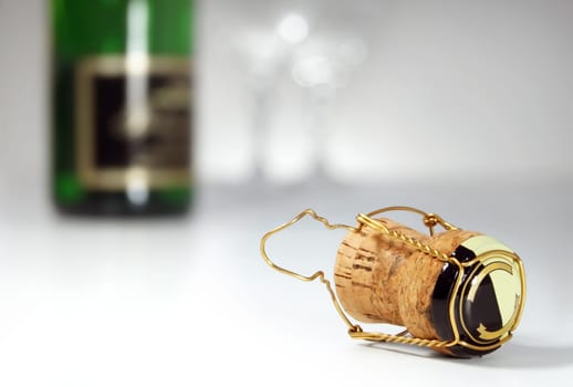 Champagne cork in foreground, bottle and glasses in background, celebration