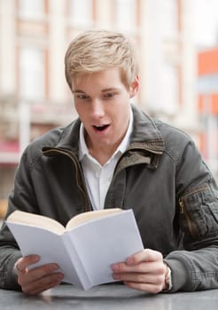 Young guy shocked while reading a book in an outdoor cafe