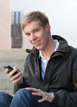 Young happy blond handsome boy holds his mobile phone