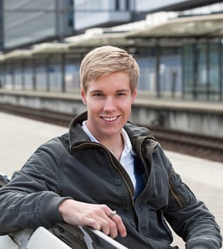 Young blond handsome guy sitting on a bench on railway station