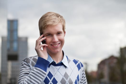 Young blond man smiles while speaking outdoors on his cellphone