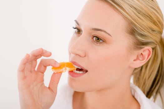 Healthy lifestyle - portrait of woman biting tangerine slice on white background