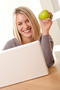 Smiling blond student working with laptop and eating apple