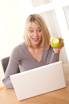 Blond student working with laptop and eating apple